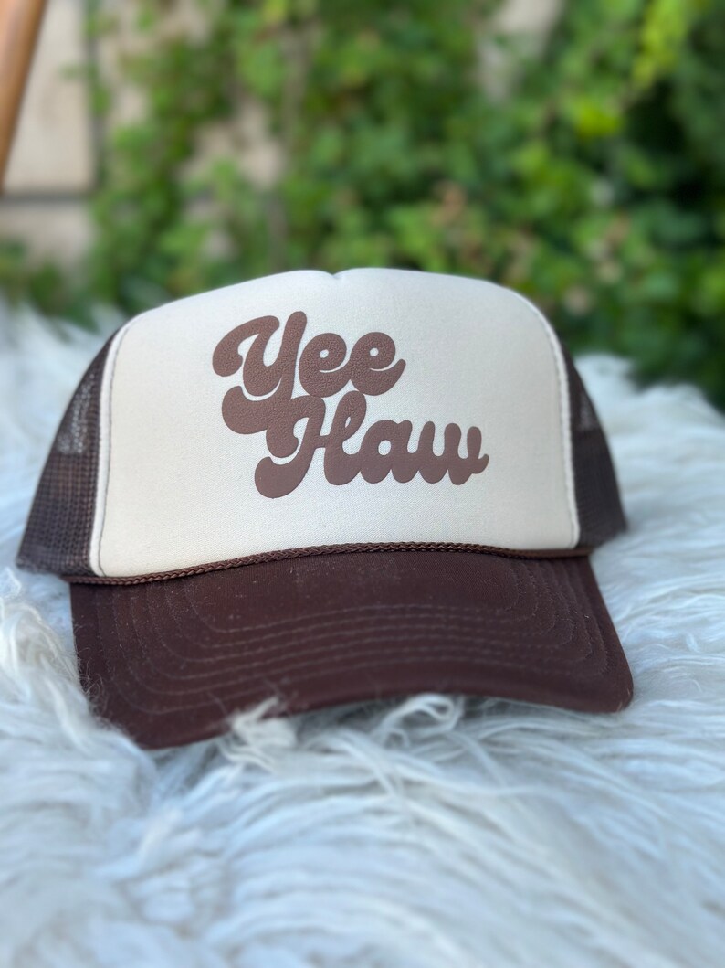 May include: A brown and white trucker hat with the text "Yee Haw" in brown script lettering.