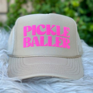 May include: A beige trucker hat with a pink "PICKLE BALLER" logo.
