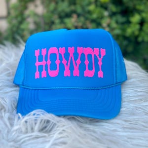 May include: A bright blue trucker hat with a pink "HOWDY" embroidered on the front.