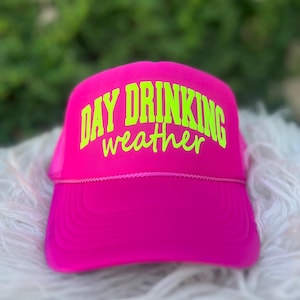 Puede incluir: Una gorra de camionero de malla rosa con un dise&ntilde;o bordado en verde ne&oacute;n que dice "Day Drinking weather".