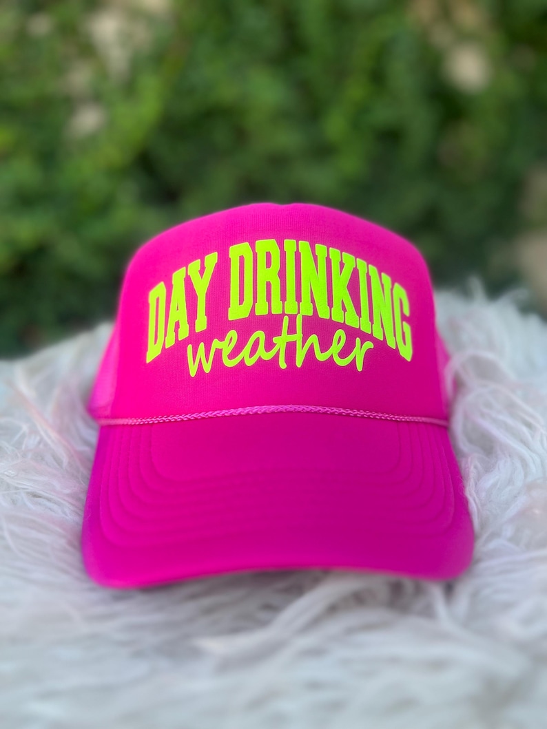 Puede incluir: Una gorra de camionero de malla rosa con un dise&ntilde;o bordado en verde ne&oacute;n que dice "Day Drinking weather".
