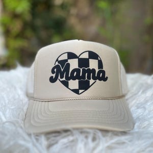 May include: A beige trucker hat with a black and white chequered heart and the word "Mama" in a retro font.