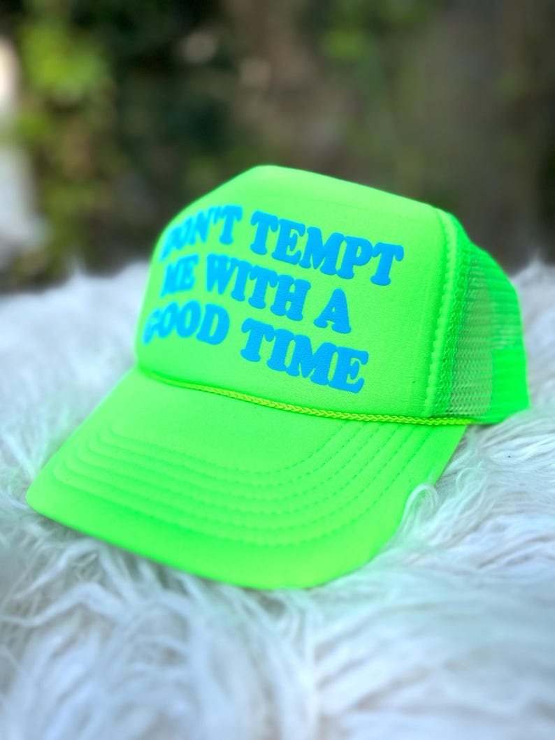 May include: A neon green trucker hat with a yellow brim and a blue inscription that reads "Don't tempt me with a good time".