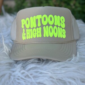 May include: A beige trucker hat with a neon green logo that says "Pontoons & High Noons".