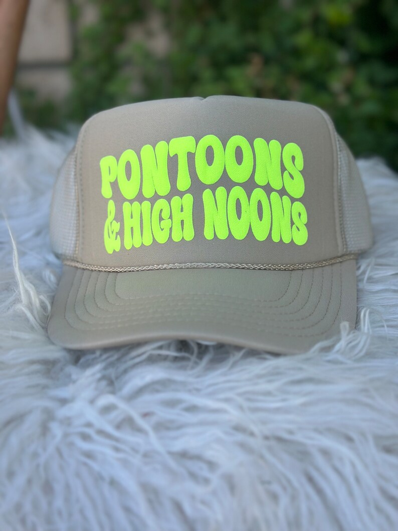 May include: A beige trucker hat with a neon green logo that says "Pontoons & High Noons".