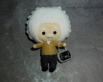 May include: A felt toy of Albert Einstein with white hair, a brown sweater, black pants, and a chalkboard that says "E=mc^2".