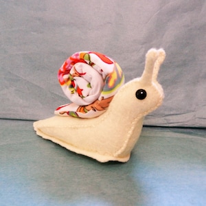 May include: A white felt snail with a colorful fabric shell. The snail has a black button eye.
