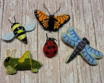 May include: Five felt insect ornaments: a yellow and black bee, a red ladybug, a green grasshopper, a blue dragonfly, and an orange and black butterfly.