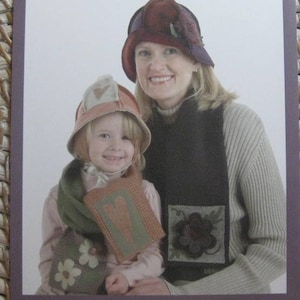 May include: A pattern for a handmade "Bundle Up!" scarf and hat set. The set features a brown scarf with a flower design and a pink hat with a heart design. The pattern is by Cathy Pendleton and is available from Indygo Junction.