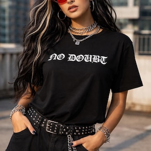 Puede incluir: Camiseta negra con el texto "NO DOUBT" en letras g&oacute;ticas blancas. La persona lleva un cintur&oacute;n con tachuelas, joyas de cadena plateada y gafas de sol rojas. El atuendo se completa con pantalones negros.