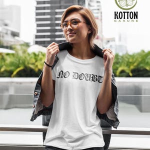 Puede incluir: Camiseta blanca con el texto "NO DOUBT" en fuente g&oacute;tica. La camiseta se lleva con una chaqueta vaquera negra y vaqueros grises. La imagen tambi&eacute;n incluye un logotipo de "Kotton Gakure".