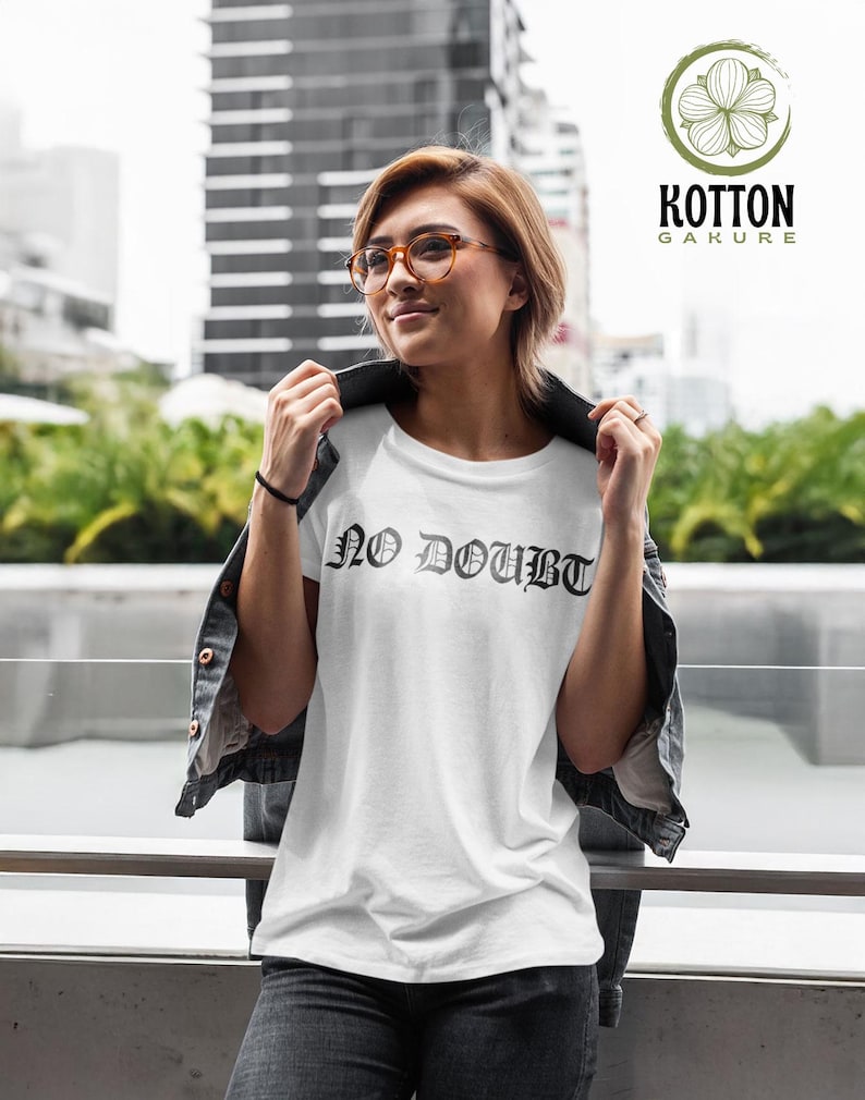 Puede incluir: Camiseta blanca con el texto "NO DOUBT" en fuente g&oacute;tica. La camiseta se lleva con una chaqueta vaquera negra y vaqueros grises. La imagen tambi&eacute;n incluye un logotipo de "Kotton Gakure".