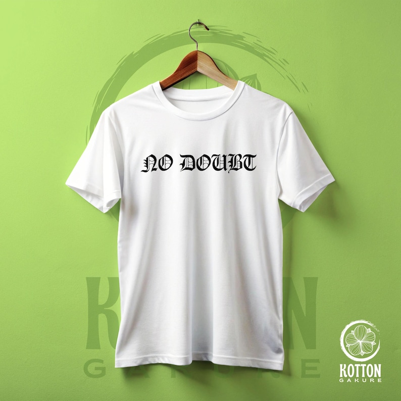 Puede incluir: Una camiseta blanca con la frase "NO DOUBT" impresa en negro con letras g&oacute;ticas. La camiseta est&aacute; colgada en una percha de madera sobre un fondo verde. Tiene mangas cortas y cuello redondo.