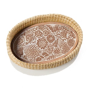 May include: Oval woven basket with a decorative floral and butterfly design. The interior features a brown and white ceramic insert with embossed flowers and butterflies. The basket is made of natural-colored woven material.