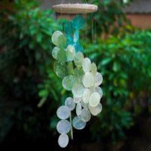 May include: A wind chime made of iridescent seashells in shades of green and white. The shells are arranged in a spiral pattern and hang from a wooden ring.