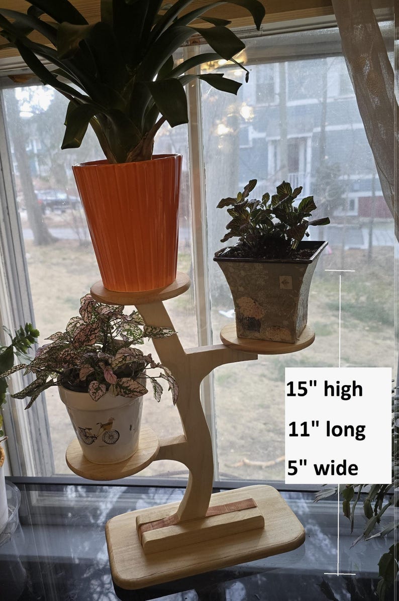 Pode incluir: Um suporte de plantas de madeira com tr&ecirc;s n&iacute;veis, segurando plantas em vasos. O suporte tem 38 cm de altura, 28 cm de comprimento e 13 cm de largura. O suporte tem um acabamento em madeira natural e um design &uacute;nico em forma de &aacute;rvore.