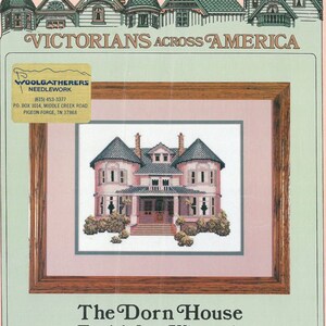 May include: Cross stitch pattern of a pink Victorian house with a wraparound porch and a gabled roof. The house is surrounded by green bushes and trees. The pattern is titled "The Dorn House, Fond du Lac, Wisconsin".