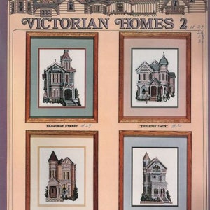 May include: Four cross-stitch patterns of Victorian homes, each framed in a light brown frame with a light blue mat. The patterns are titled "Broadway Street", "The Pink Lady", "Oak Street", and "Pierce Street".