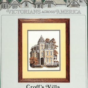 May include: A framed cross-stitch pattern of a Victorian-style house with a brown wooden frame and a yellow mount. The house is white with brown trim and has a large porch. The text "Croff's Villa" and "Rhinebeck, New York" is printed below the image.