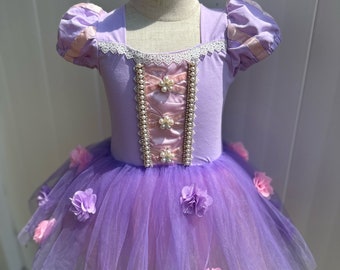 May include: Purple tulle tutu dress with pink flower accents and a lavender bodice with pearl embellishments. The bodice has a lace trim and a pink ribbon.