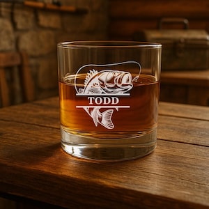 May include: A clear glass rocks glass with a design of a bass fish and the name "TODD" etched on the front. The glass is filled with amber liquid.