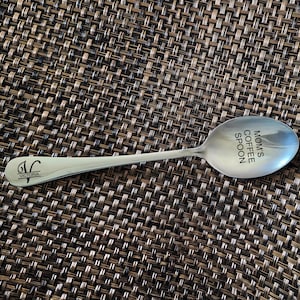 May include: A silver coffee spoon with the text "Mom's Coffee Spoon" engraved on the bowl. The handle has the letter "V" and the word "Victoria" engraved on it.
