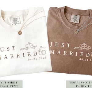 May include: Two Comfort Colors t-shirts, one ivory and one espresso, with the text "JUST MARRIED" and a car graphic. Each shirt has a necklace with a pendant. The date "04.31.2026" is printed below the text.