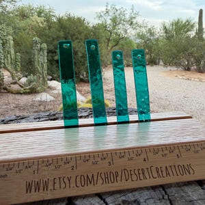 Puede incluir: Cuatro piezas rectangulares de vidrio color verde azulado con superficies texturizadas y un solo orificio en la parte superior de cada una. Están colocadas en un soporte de madera con una regla en pulgadas y el texto WWW.ETSY.COM/SHOP/DESERTCREATIONS.