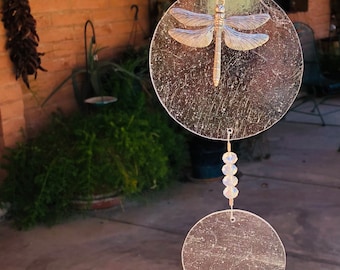 May include: A hanging suncatcher featuring a silver-toned dragonfly charm centered on a clear circular disc. Below this, a smaller clear disc is connected by a string of clear faceted beads, ending in a large, clear, multi-faceted crystal sphere.