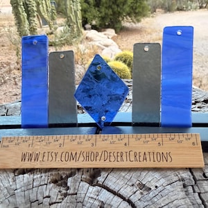 May include: A collection of glass art pieces in shades of blue and gray, including rectangular and diamond shapes. The pieces are displayed on a black base with a wooden ruler that reads "www.etsy.com/shop/DesertCreations".