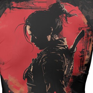 Peut inclure: Un t-shirt graphique noir et rouge présentant une illustration stylisée d'une personne aux cheveux en chignon décoiffé, portant une armure et une épée dans le dos. Le motif est placé sur un grand fond circulaire rouge aux textures usées.