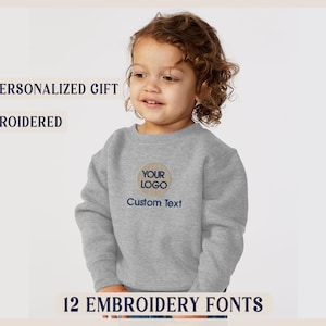 May include: A gray sweatshirt with a round embroidered patch that says "Your Logo" and "Custom Text". The sweatshirt is a personalized gift and is embroidered.