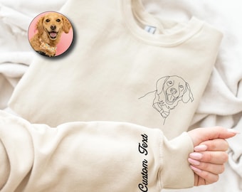 May include: Cream-colored sweatshirt with a black line drawing of a dog and a circular photo of a dog. The word "Embroidered" is in the upper left corner. The sleeve has the words "Custom Text" in a script font.