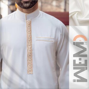 May include: White long-sleeve shirt with a gold embroidered design down the front. The shirt has a stand-up collar and a pocket on the left side. The fabric is smooth and has a slight sheen.