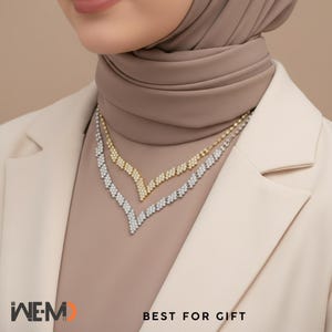 May include: Two V-shaped necklaces, one in gold tone and one in silver tone, each featuring a series of small, clear, sparkling stones set in a chevron pattern. The necklaces are layered, with the gold tone piece resting above the silver tone piece.