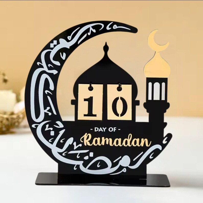 May include: Black metal Ramadan calendar with a crescent moon, mosque, and lantern design. The calendar features a flip-style design with the number 10 displayed. The text "Day of Ramadan" is written below the calendar.