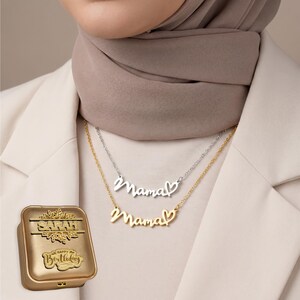 May include: Two necklaces with the word "Mama" in cursive script, each with a heart accent. One necklace is gold-toned, the other silver-toned. A gold-colored box with the name "Sarah" and "Happy Birthday" is also visible.