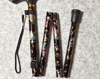 May include: A black folding walking cane with a floral pattern in pink, green, and yellow. The cane has a black handle and wrist strap. When folded, the cane is approximately 34 inches long.