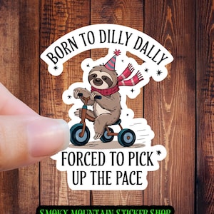 May include: A sticker featuring a cartoon sloth wearing a party hat and scarf, riding a tricycle. The text reads "Born to Dilly Dally * Forced to Pick * Up the Pace" and "Smoky Mountain Sticker Shop".