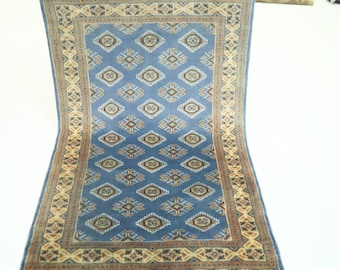 May include: A blue rug with a geometric pattern in shades of brown and beige. The rug has a border with a repeating design.