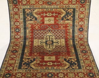 Könnte beinhalten: Ein traditioneller Teppich in Rot-, Blau- und Goldtönen. Der Teppich hat ein zentrales Medaillon mit komplizierten geometrischen Mustern und einen Rand mit floralen Motiven.
