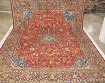 May include: A large, intricately patterned rug with a red background and blue and cream accents. The rug has a central medallion and a border with floral and geometric designs.