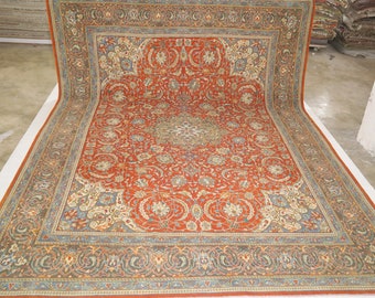 May include: A large, intricately patterned rug with a red background and a blue and cream border. The rug features a central medallion with floral and geometric designs.