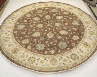 May include: A round rug with a brown center and a cream-colored border. The center features a floral pattern with brown, cream, and green colors. The border has a repeating floral design with yellow, cream, and brown accents.