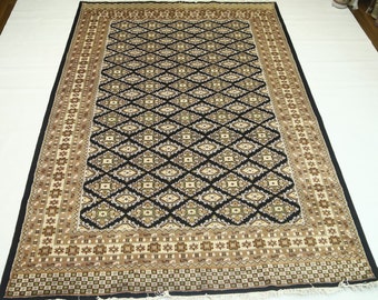 Puede incluir: Una alfombra de color negro y crema con un diseño geométrico. La alfombra tiene un borde marrón y crema con flecos negros.