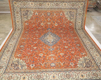 May include: A large, intricately patterned rug with a central medallion in shades of blue, cream, and red. The rug has a rich, orange background with floral and geometric designs throughout.