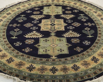 May include: A round rug with a navy blue center and a beige and green border. The center features a geometric pattern with stars and other shapes. The border has a repeating pattern of stars and other shapes.