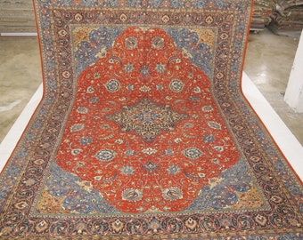 May include: A large, intricately patterned rug with a red background and blue and beige accents. The rug has a central medallion and a border with floral and geometric designs.