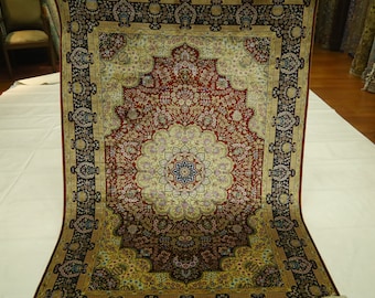 May include: An elaborate Persian rug with a central medallion design. The rug displays a rich colour palette of red, gold, and black, with intricate floral patterns and a detailed border. The rug is displayed on a white surface.