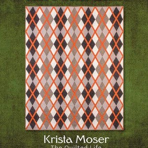 May include: A rectangular quilt featuring a repeating argyle diamond pattern in shades of dark gray, light gray, and white, accented by bright orange lines. The text ARGYLE LAD appears at the top, and Krista Moser The Quilted Life at the bottom.